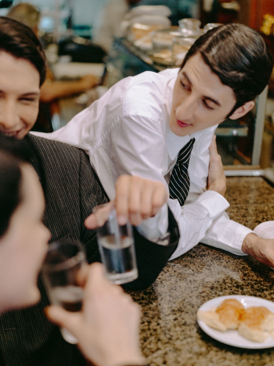 A waiter in shirt and tie leaning over the bar, chatting to regulars