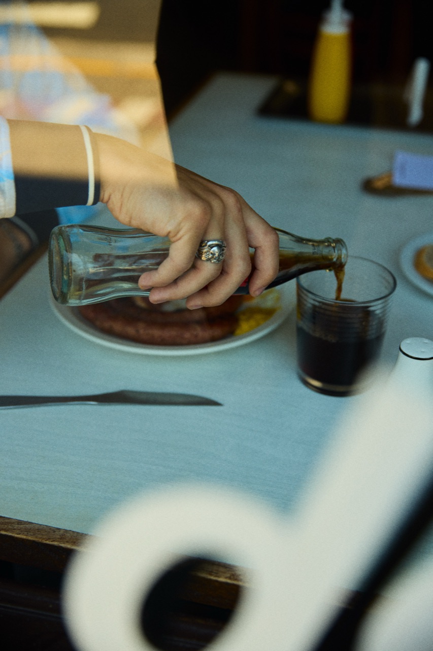 A hand pouring cola from a glass bottle by the window