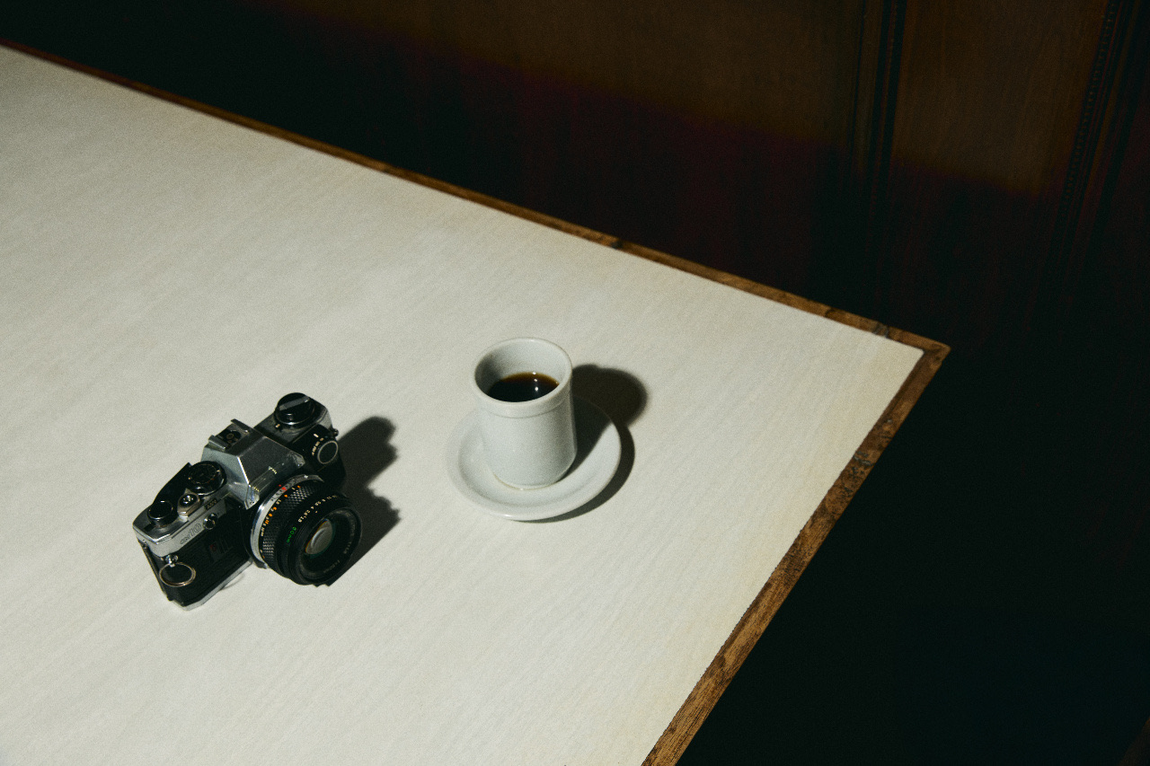 A film camera and an espresso on the corner of a white table