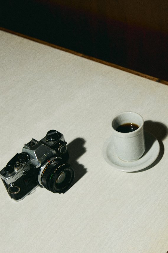 An espresso and a film camera on a white table in a dark café