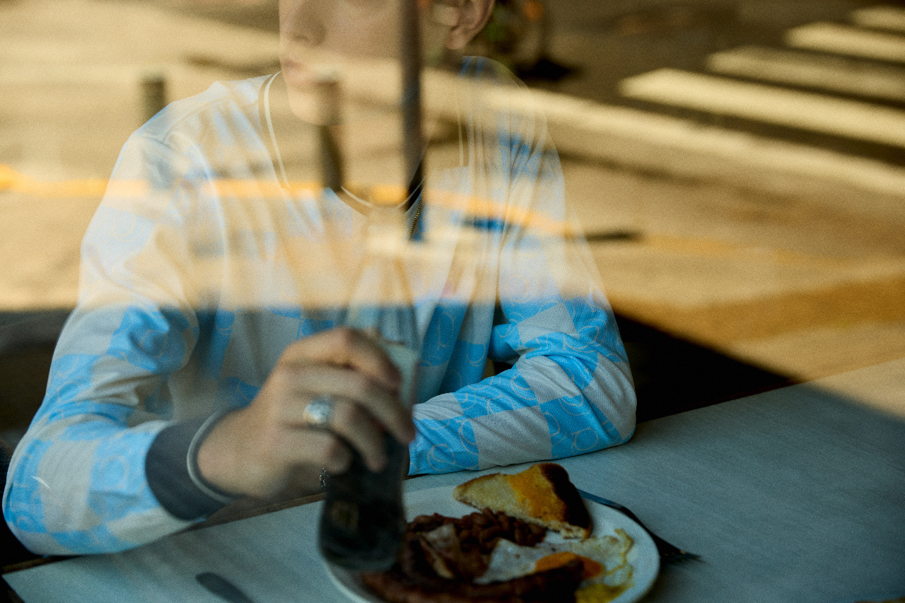 Someone in a striped shirt at a window table, seen through reflections